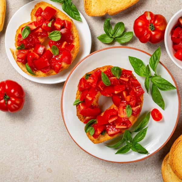 Two plates of Italian bruschetta with fresh diced tomatoes and basil, surrounded by ingredients.