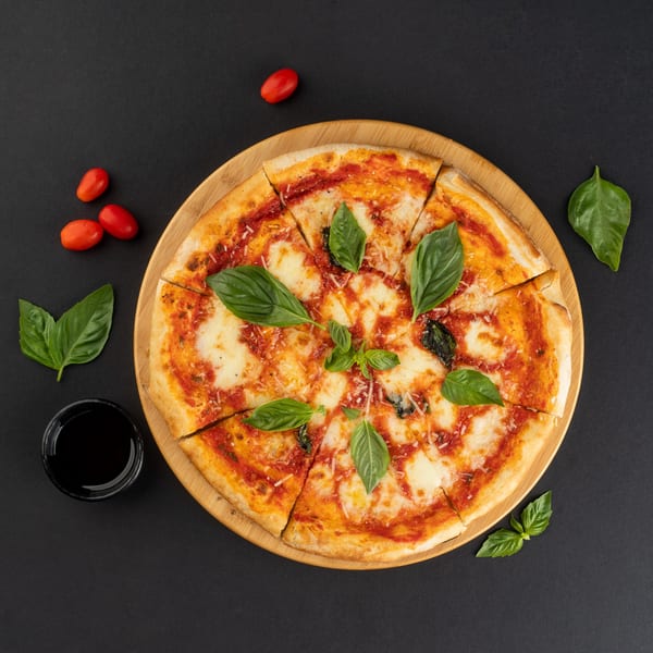 A sliced Margherita pizza on a wooden board, garnished with fresh basil, cherry tomatoes, and a drink.