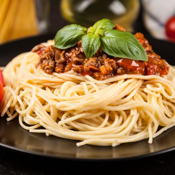 Celeno's Bistro's spaghetti bolognese, topped with fresh basil, on a black plate.