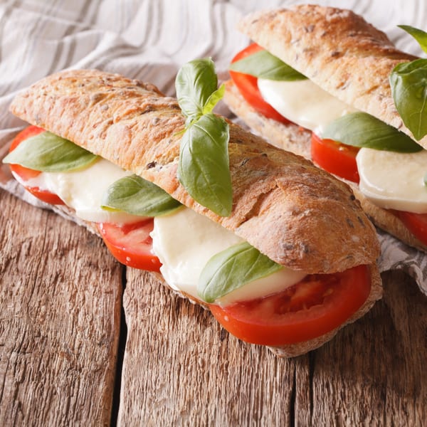 Two fresh Italian caprese sandwiches with mozzarella, tomatoes, and basil on a wooden table.